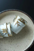 Load image into Gallery viewer, Tongxin She Teahouse Selection | Creamy White Gilded Bamboo Teacups Snow-white porcelain adorned with bamboo painted in gilded pigment.
A gilded rim encircles the cup, freezing tranquil time upon the vessel.