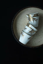 Load image into Gallery viewer, Tongxin She Teahouse Selection | Creamy White Gilded Bamboo Teacups Snow-white porcelain adorned with bamboo painted in gilded pigment.
A gilded rim encircles the cup, freezing tranquil time upon the vessel.
