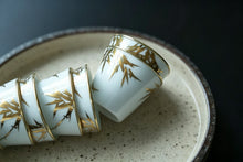Load image into Gallery viewer, Tongxin She Teahouse Selection | Creamy White Gilded Bamboo Teacups Snow-white porcelain adorned with bamboo painted in gilded pigment.
A gilded rim encircles the cup, freezing tranquil time upon the vessel.
